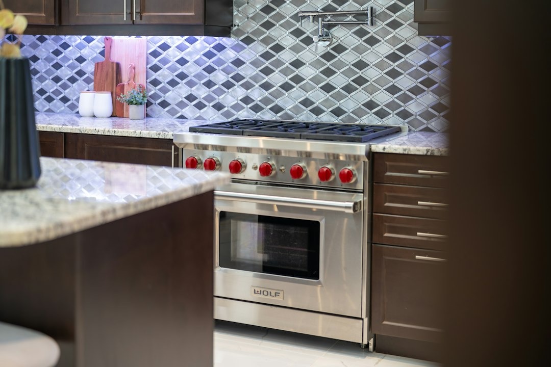 Stainless steel range with red knobs in a modern kitchen.